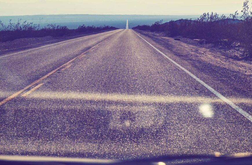 A long dry highway as seen through a windshield.